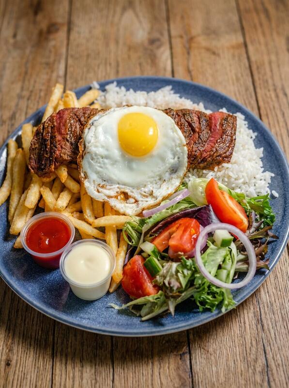 Redondos churrasco premium platter with grilled steak fried egg white rice french fries and fresh salad on blue plate