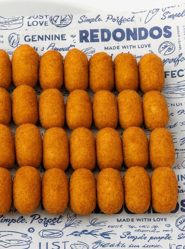 Golden crispy Spanish croquettes lined up on Redondos branded wrapping paper — Manchego cheese Ibérico ham and chicken varieties